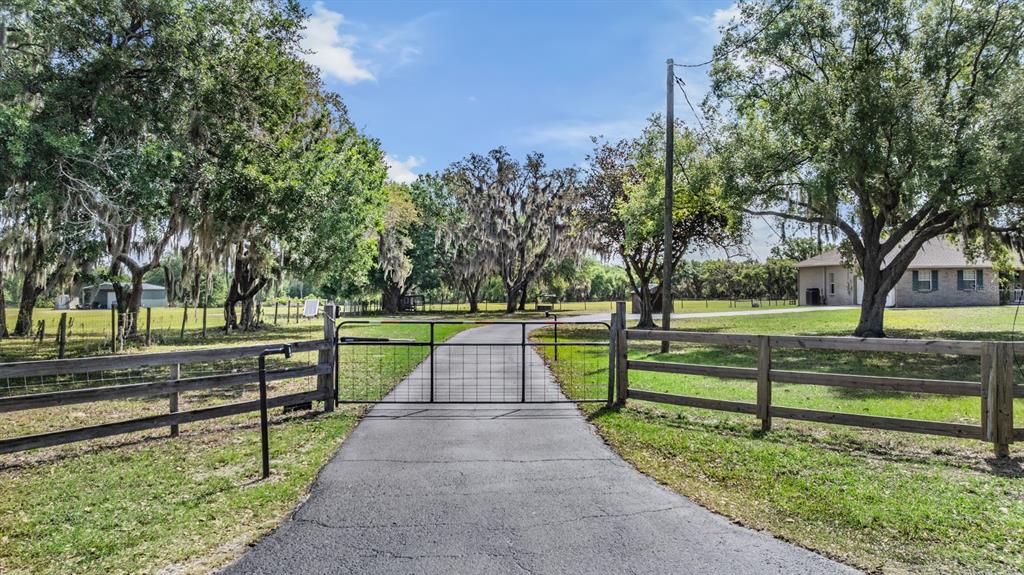 A paved driveway leads through a metal gate toward a house on a grassy lot — 17216 ALDERMAN TURNER ROAD, WIMAUMA, FL
