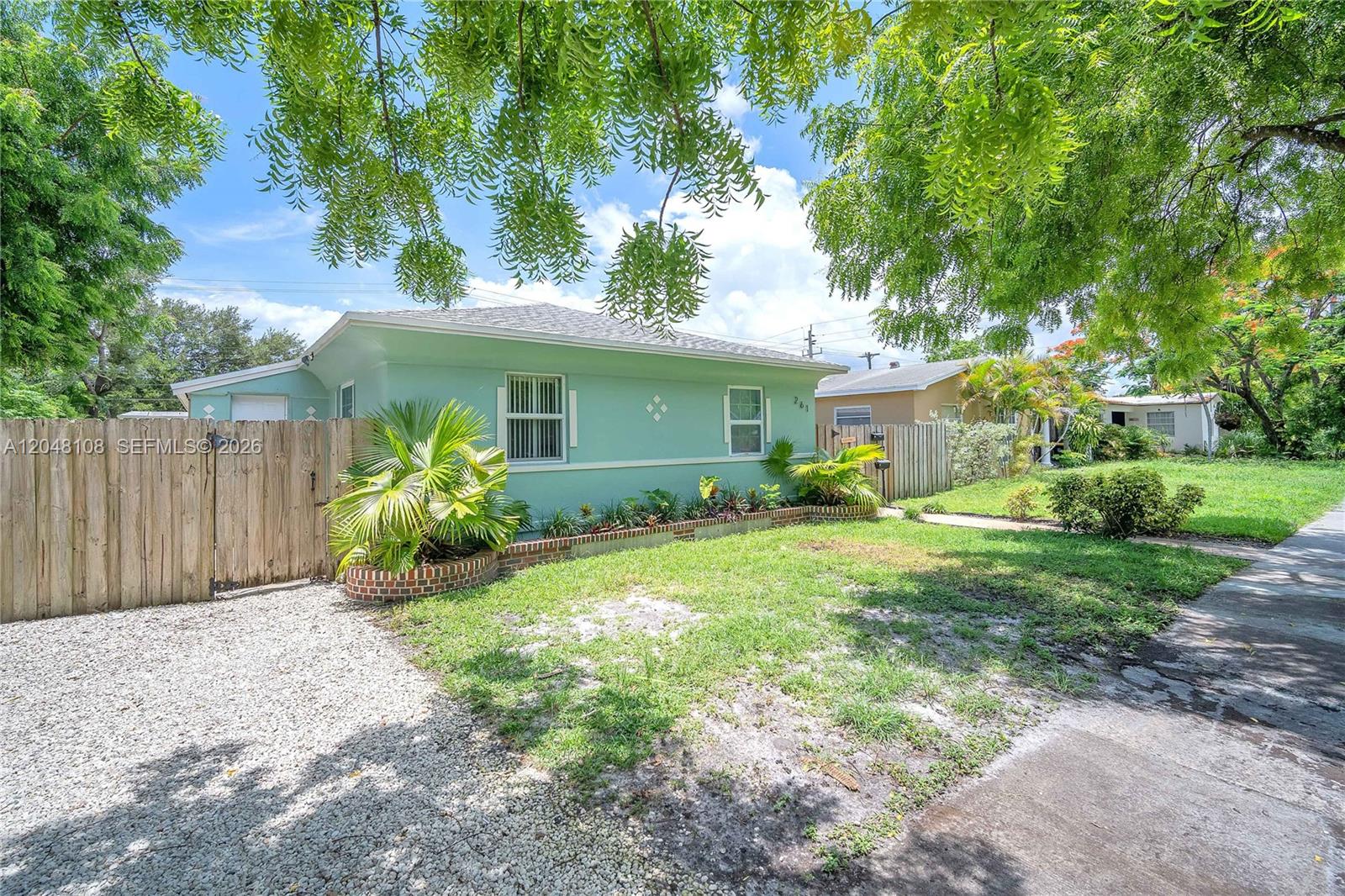 A light green single-story house features a gravel driveway, wooden fence, and mature trees — 261 SW 15th St # 2, Dania Beach FL 33004, DANIA BEACH, FL
