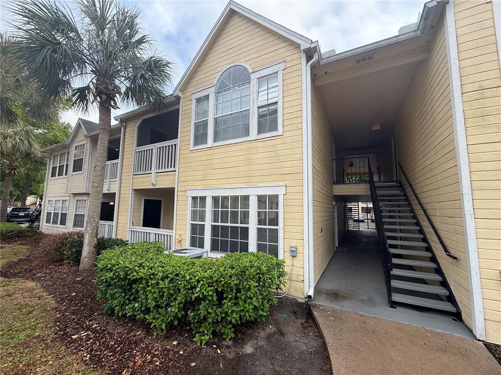 A two-story yellow apartment building features a staircase leading to an upper-level balcony — 1025 S HIAWASSEE ROAD UNIT 2216, ORLANDO, FL