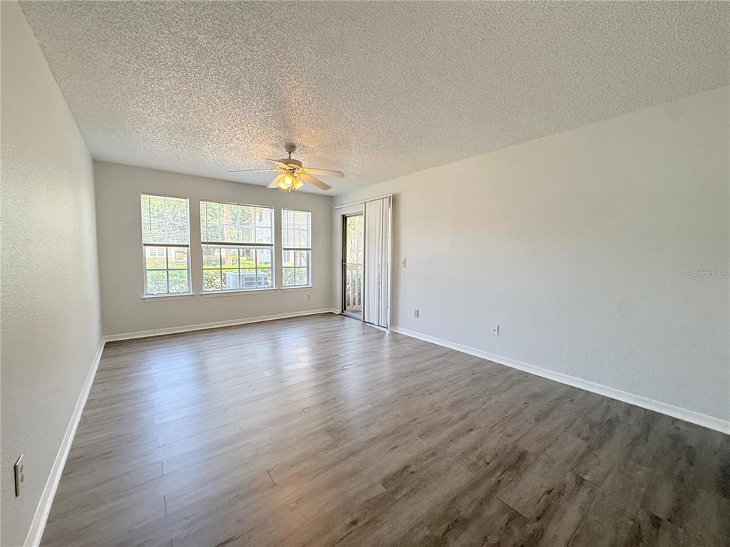 An empty living room features light gray walls, wood-look flooring, a ceiling fan, and windows — 1025 S HIAWASSEE ROAD UNIT 2216, ORLANDO, FL
