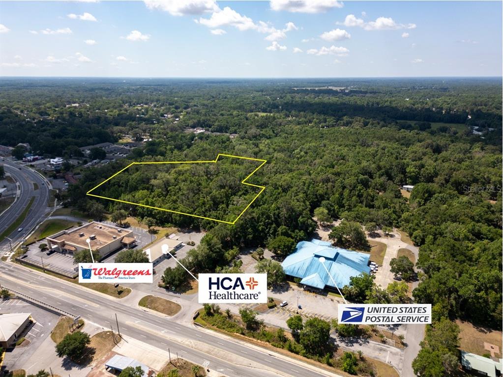 An aerial view shows a wooded lot outlined in yellow adjacent to commercial buildings — 11090 SE 55TH AVENUE ROAD, BELLEVIEW, FL