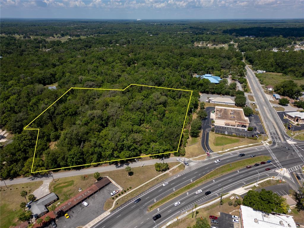 An aerial view shows a wooded lot outlined in yellow next to a commercial building — 11090 SE 55TH AVENUE ROAD, BELLEVIEW, FL