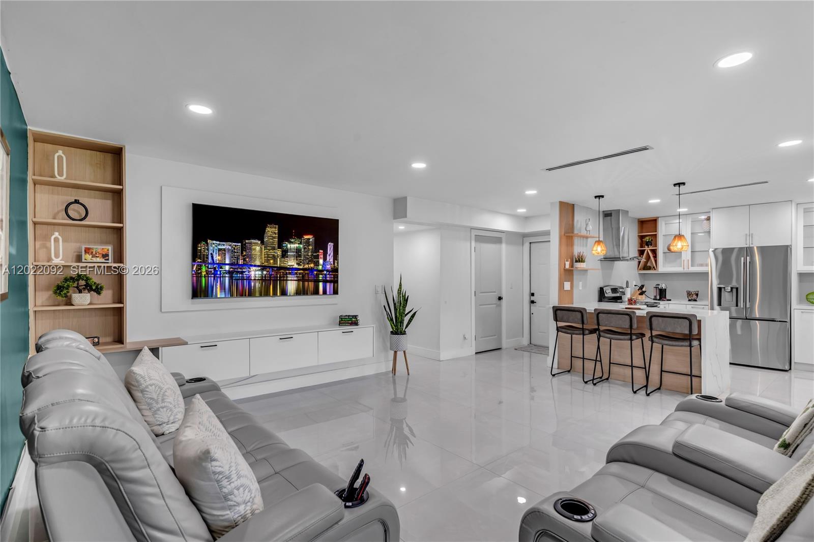 A modern open-concept living room features a grey leather sofa, wall-mounted television, and kitchen island — 17105 SW 113th Ct # 11531E, Miami FL 33157, MIAMI, FL