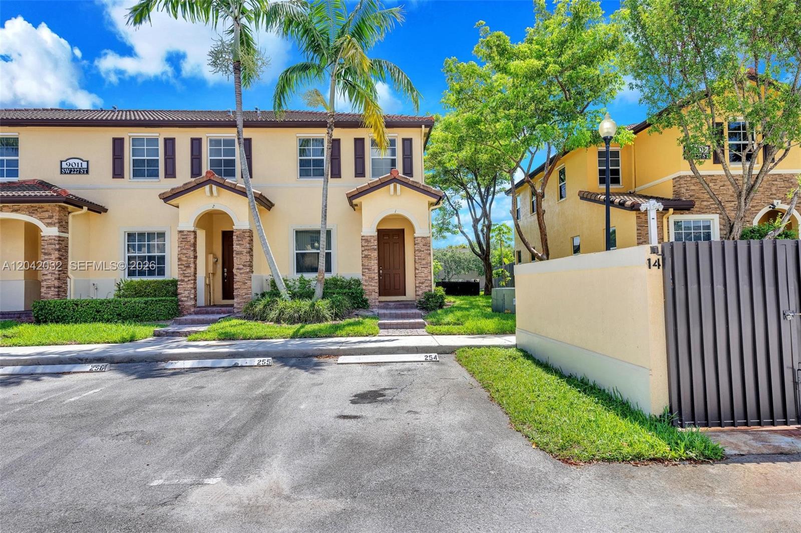 A two-story yellow townhouse exterior features stone accents, brown shutters, and assigned parking spaces — 9011 SW 227th St # 1, Cutler Bay FL 33190, CUTLER BAY, FL