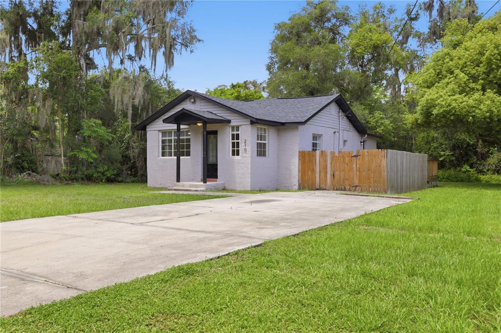 A small, light-colored single-story house with a concrete driveway and a wooden fence — 210 WINSLOW AVENUE, DELAND, FL