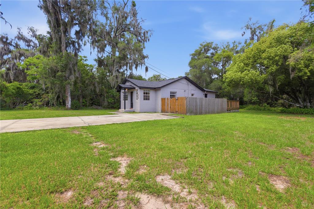 A small, light-colored house with a wooden fence sits on a large, grassy lot — 210 WINSLOW AVENUE, DELAND, FL