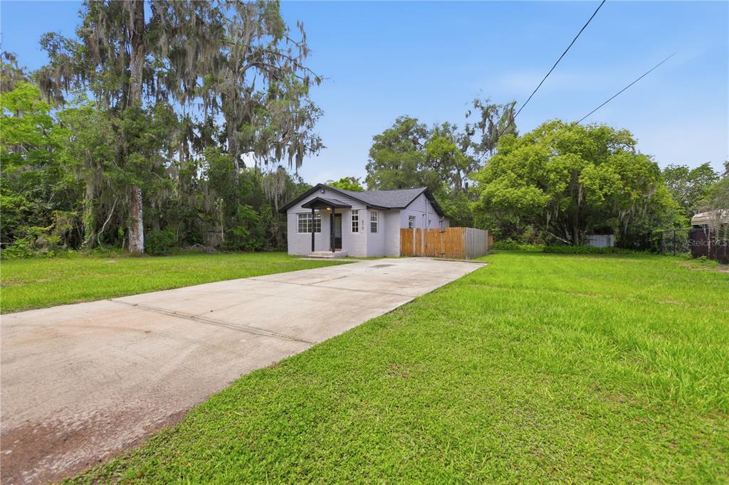 A small, light-colored house with a concrete driveway sits on a large, grassy lot — 210 WINSLOW AVENUE, DELAND, FL