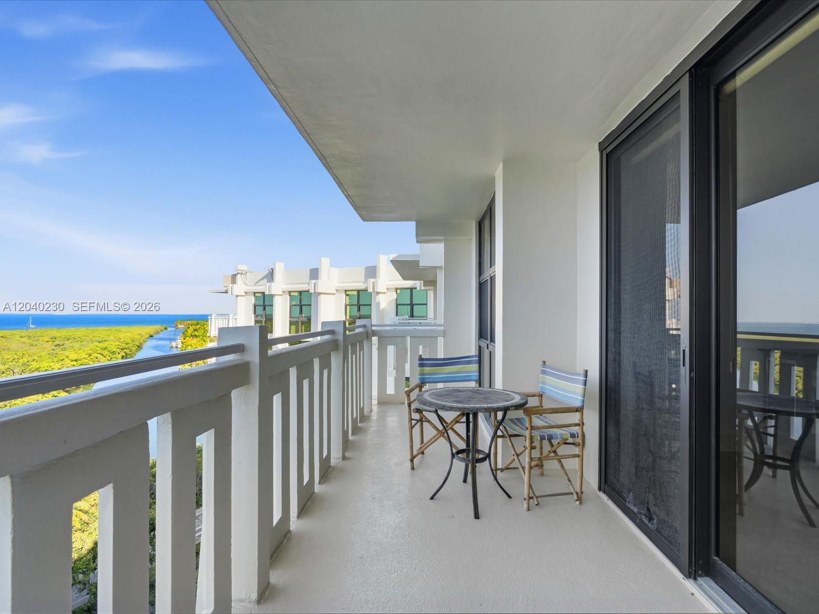 A balcony with a small table and two chairs overlooks a waterway and greenery — 1121 Crandon Blvd # E1205, Key Biscayne FL 33149, KEY BISCAYNE, FL
