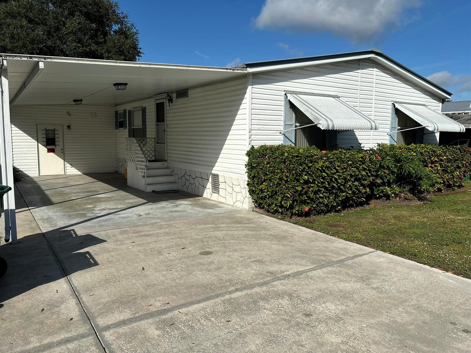 A white mobile home with a carport, concrete driveway, and a hedge in the front — 111 NE 8th Avenue, Okeechobee FL 34972, OKEECHOBEE, FL