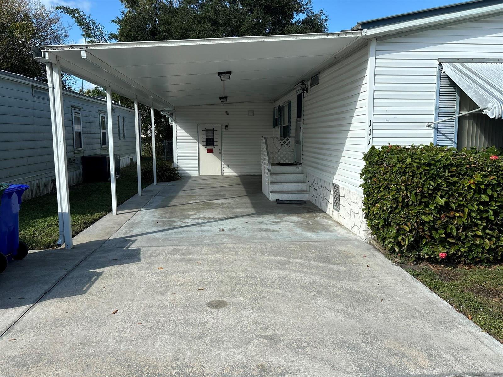 A concrete driveway leads to a covered carport and the entrance of a mobile home — 111 NE 8th Avenue, Okeechobee FL 34972, OKEECHOBEE, FL