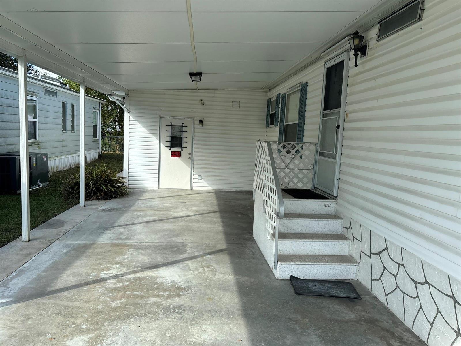 A concrete carport leads to a white mobile home with stairs and a side door — 111 NE 8th Avenue, Okeechobee FL 34972, OKEECHOBEE, FL