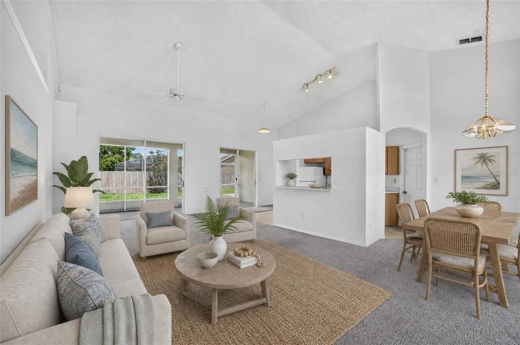 A living room and dining area with vaulted ceilings, neutral carpet, and a pass-through kitchen — 3832 BLACKBERRY CIRCLE, ST CLOUD, FL