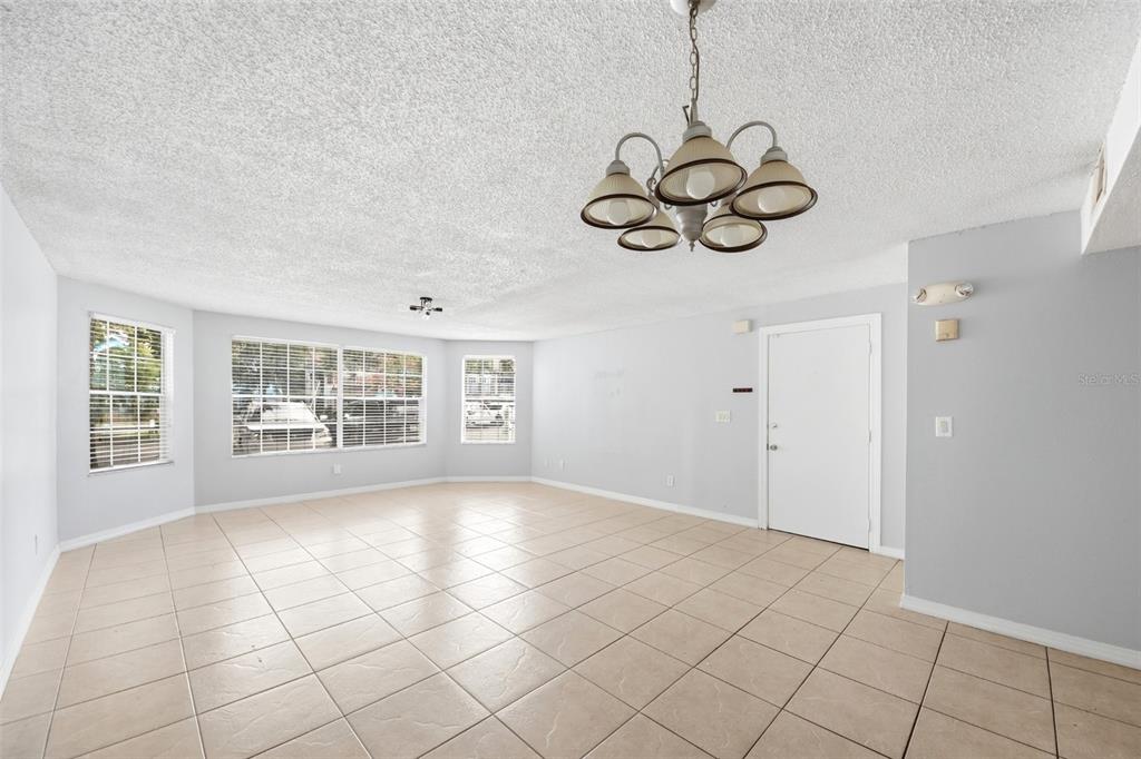 A bright, empty living room features light-colored tile flooring, a chandelier, and large windows — 2723 N POINCIANA BOULEVARD UNIT 153, KISSIMMEE, FL