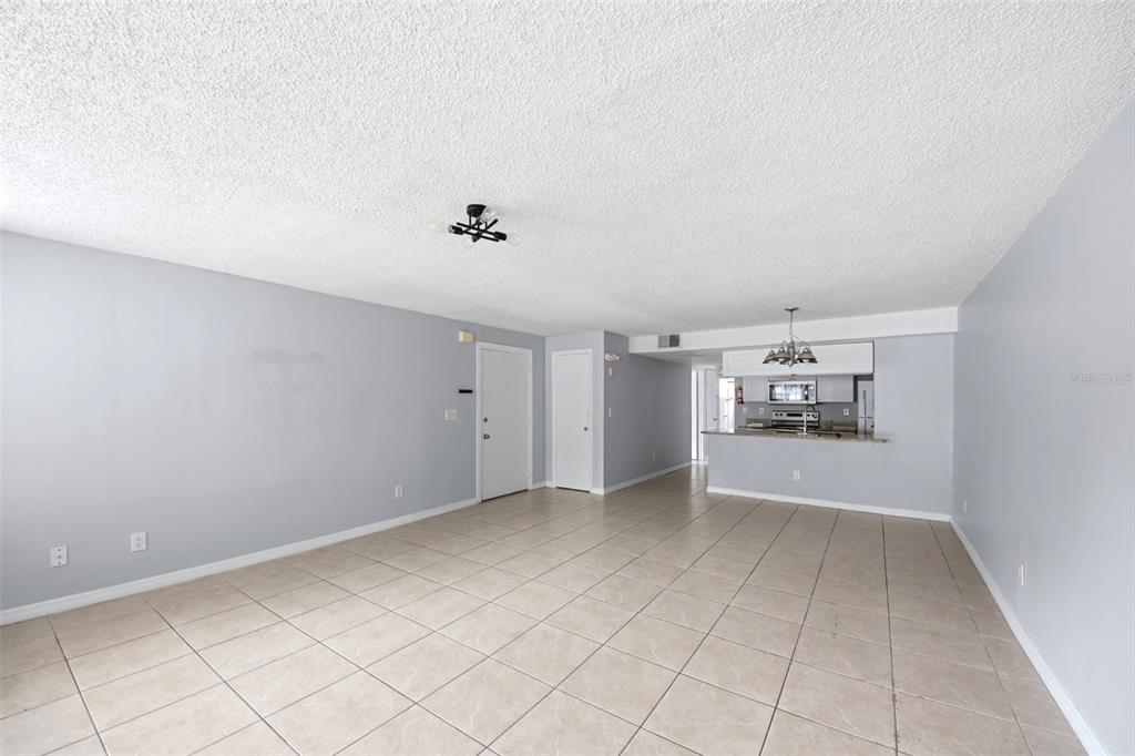 An open-concept living area with light gray walls, tiled floors, and an adjacent kitchen — 2723 N POINCIANA BOULEVARD UNIT 153, KISSIMMEE, FL
