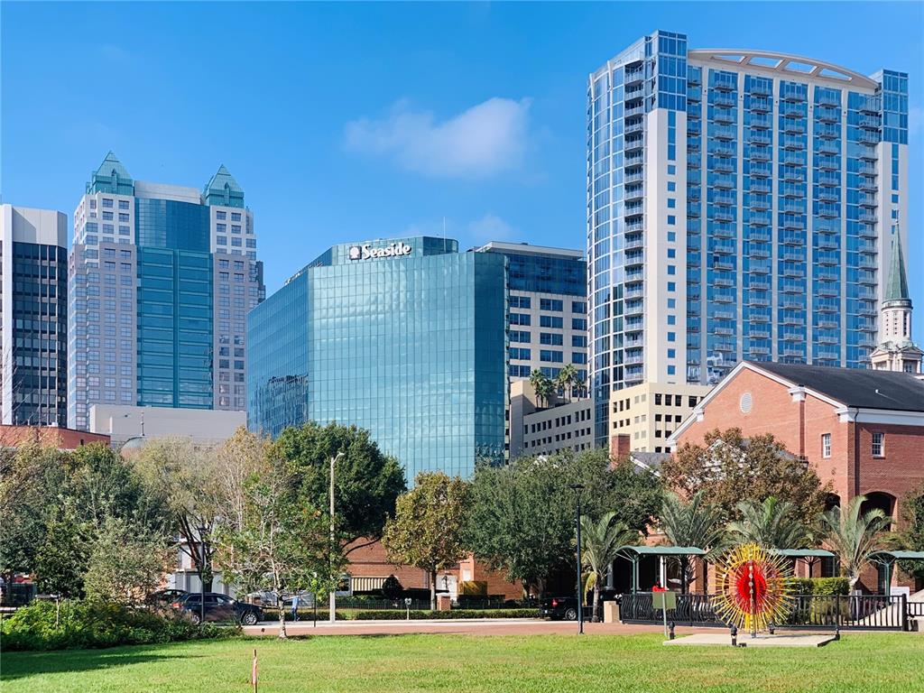 A view of a city park with modern skyscrapers and a brick building in the background — 155 S COURT AVENUE UNIT 1415, ORLANDO, FL