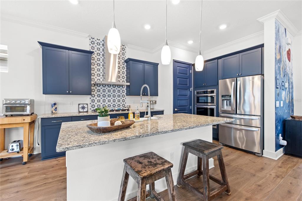 A kitchen features blue cabinets, granite countertops, a central island, and stainless steel appliances — 1234 CANYON CREEK TRAIL, WINTER GARDEN, FL