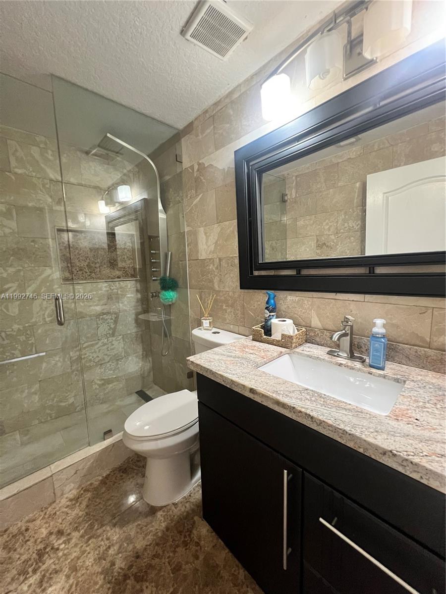 A bathroom features a glass-enclosed shower, a dark vanity with granite countertop, and stone tiling — 5513 SW 164th Ct, Miami FL 33185, MIAMI, FL