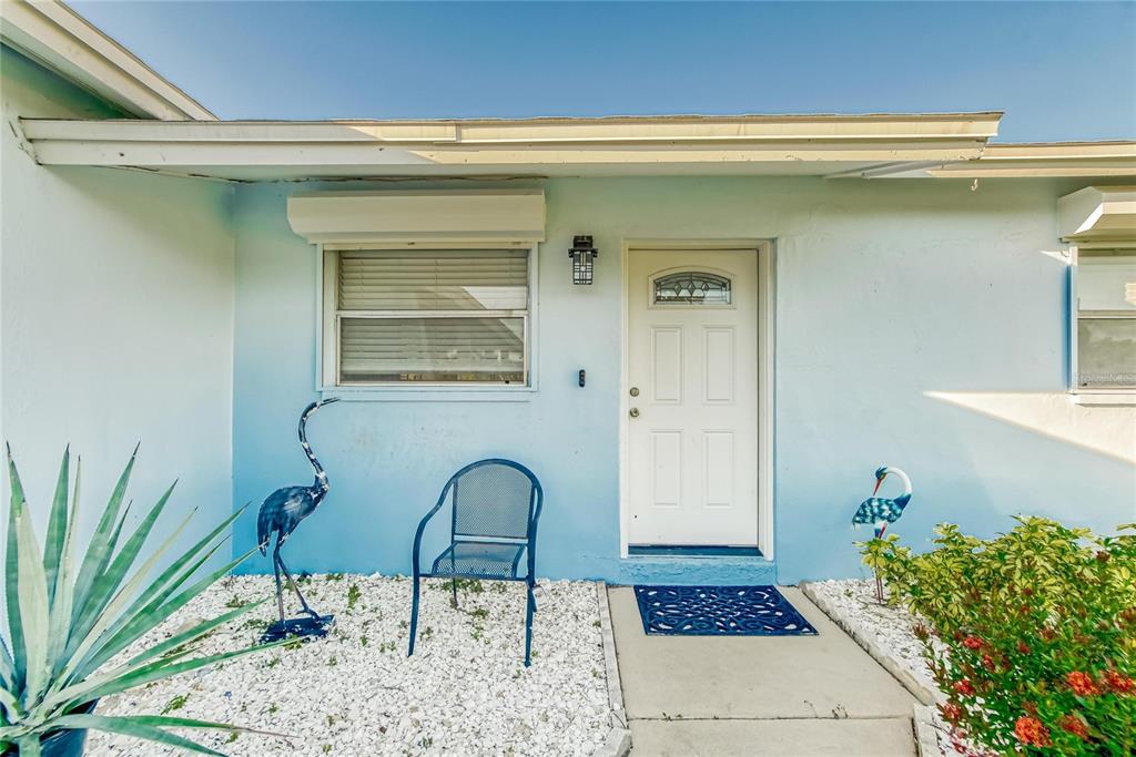 The exterior of a light blue house features a white front door and a metal chair — 6004 GOLF AND SEA BOULEVARD, APOLLO BEACH, FL