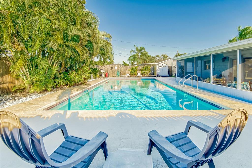 A swimming pool sits in a backyard patio area with two blue chairs in the foreground — 6004 GOLF AND SEA BOULEVARD, APOLLO BEACH, FL