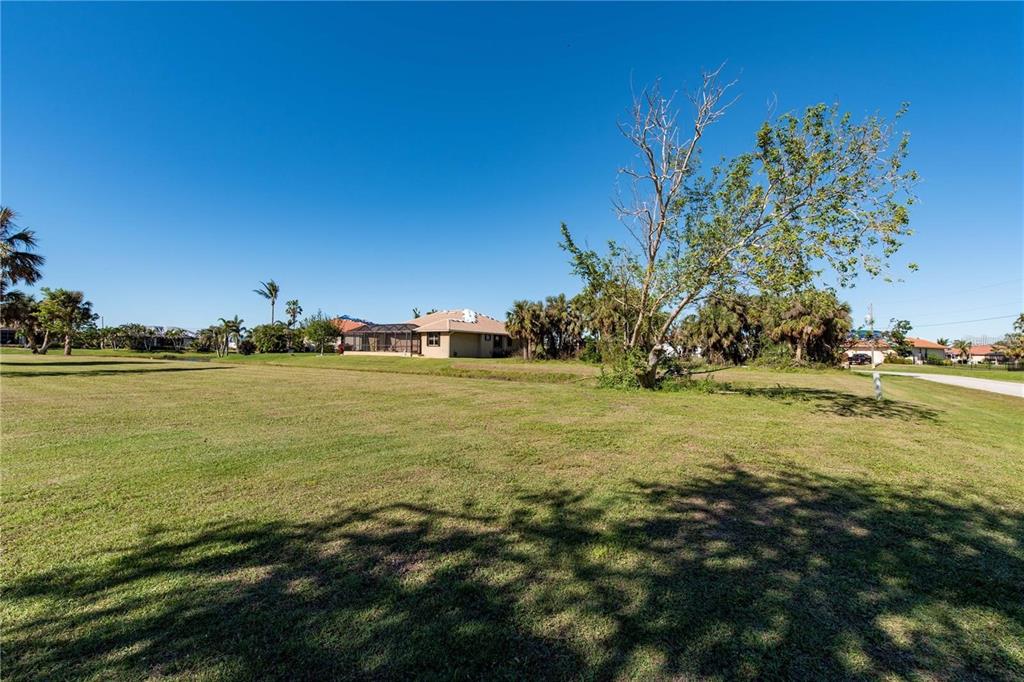 A large, grassy vacant lot sits in front of a single-story house with a pool cage — 17207 MINT LANE, PUNTA GORDA, FL