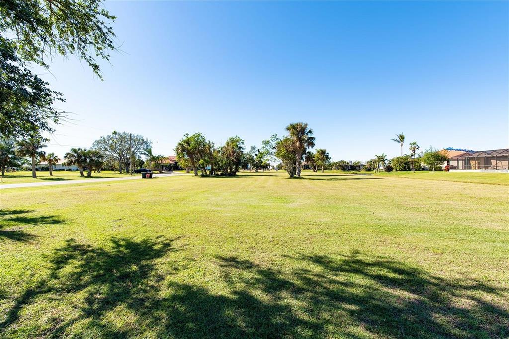 A large, flat, grassy vacant lot with scattered trees under a clear blue sky — 17207 MINT LANE, PUNTA GORDA, FL