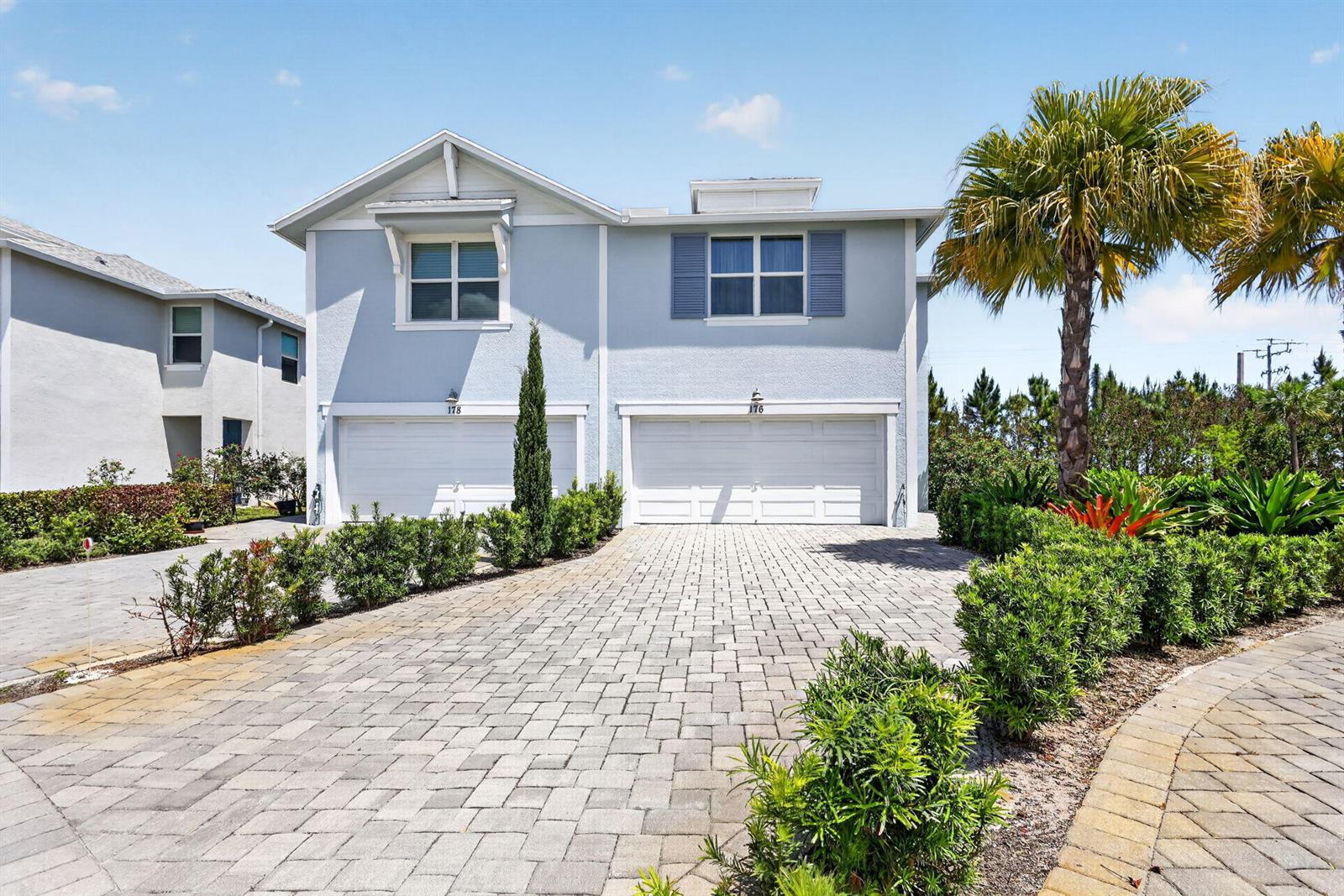 A two-story duplex with light blue siding, white garage doors, and a paved driveway — 176 Osprey Preserve Boulevard, Jensen Beach FL 34957, JENSEN BEACH, FL