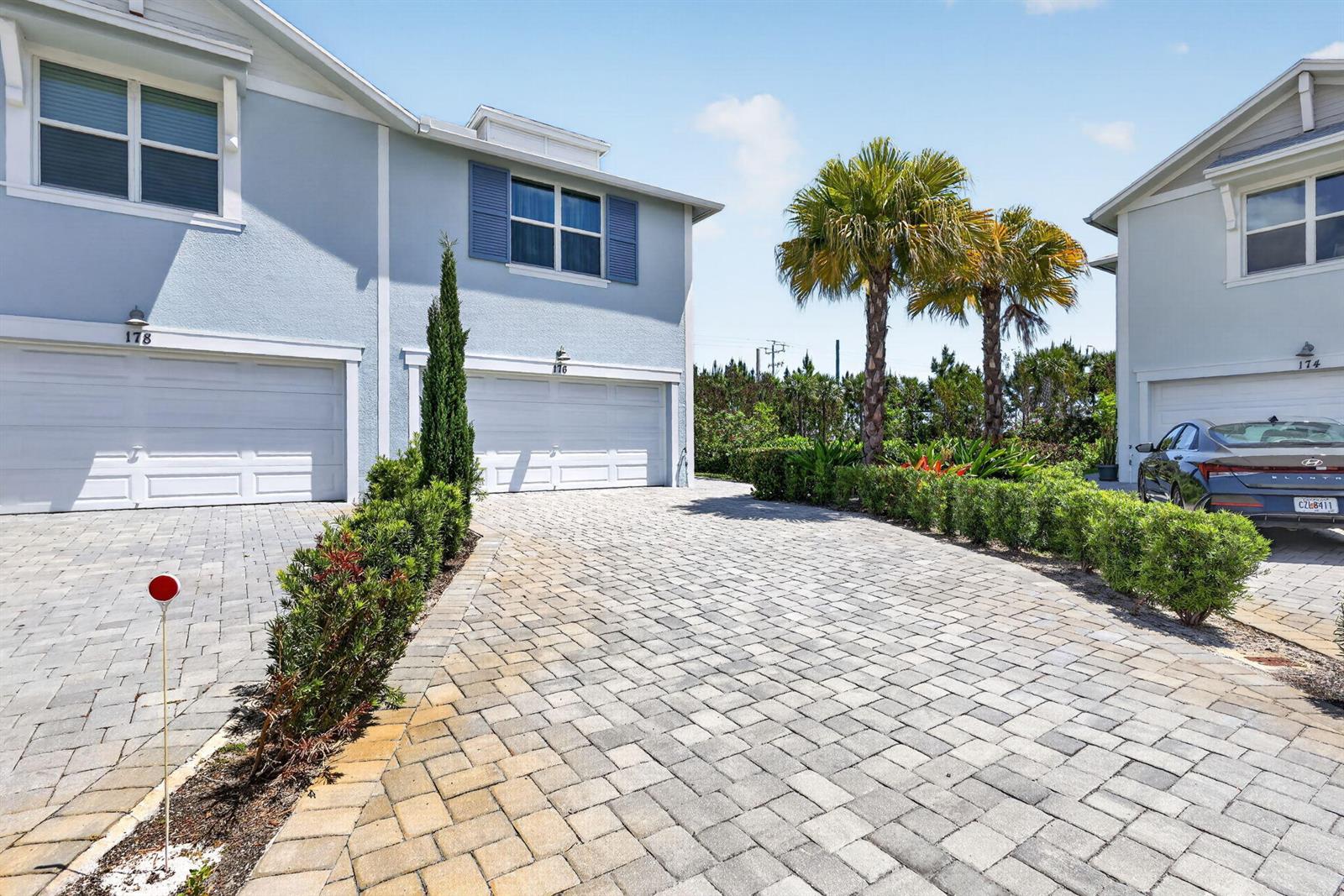 A paved driveway leads to the garages of two light blue townhomes with palm trees — 176 Osprey Preserve Boulevard, Jensen Beach FL 34957, JENSEN BEACH, FL