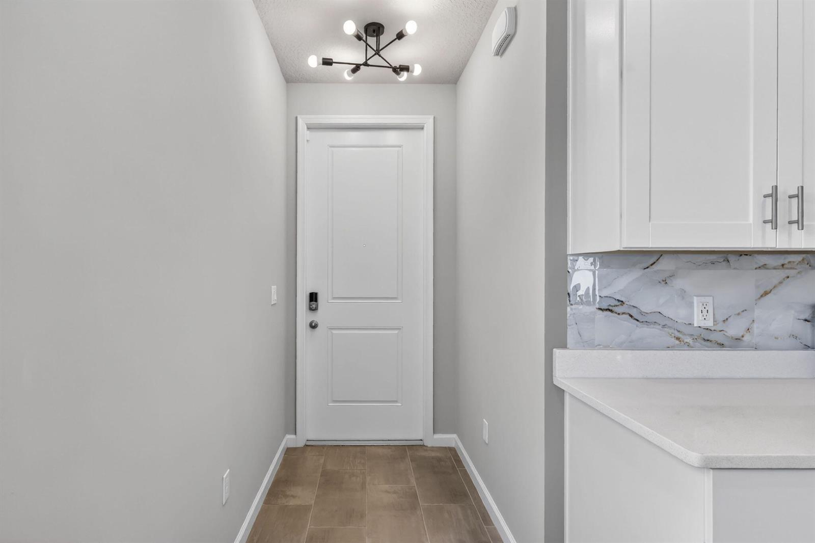 A hallway features a white door, light tile flooring, and a modern sputnik ceiling light — 176 Osprey Preserve Boulevard, Jensen Beach FL 34957, JENSEN BEACH, FL