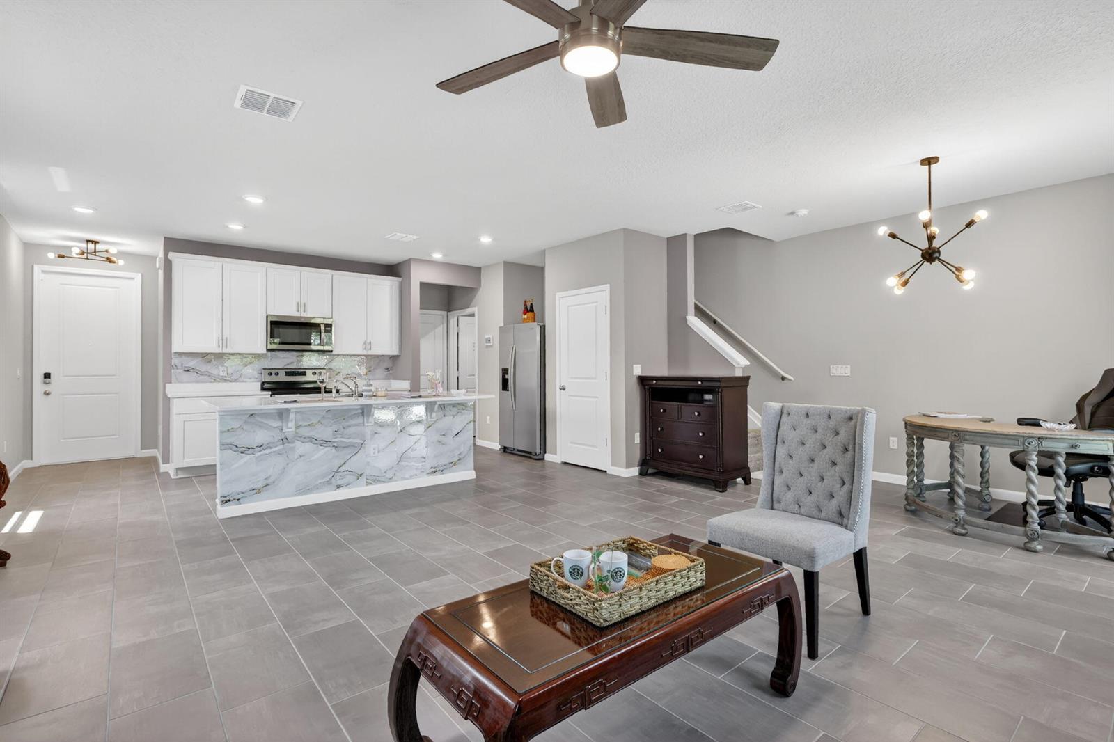 An open-concept kitchen and living area features gray tile flooring, white cabinetry, and marble-patterned counters — 176 Osprey Preserve Boulevard, Jensen Beach FL 34957, JENSEN BEACH, FL