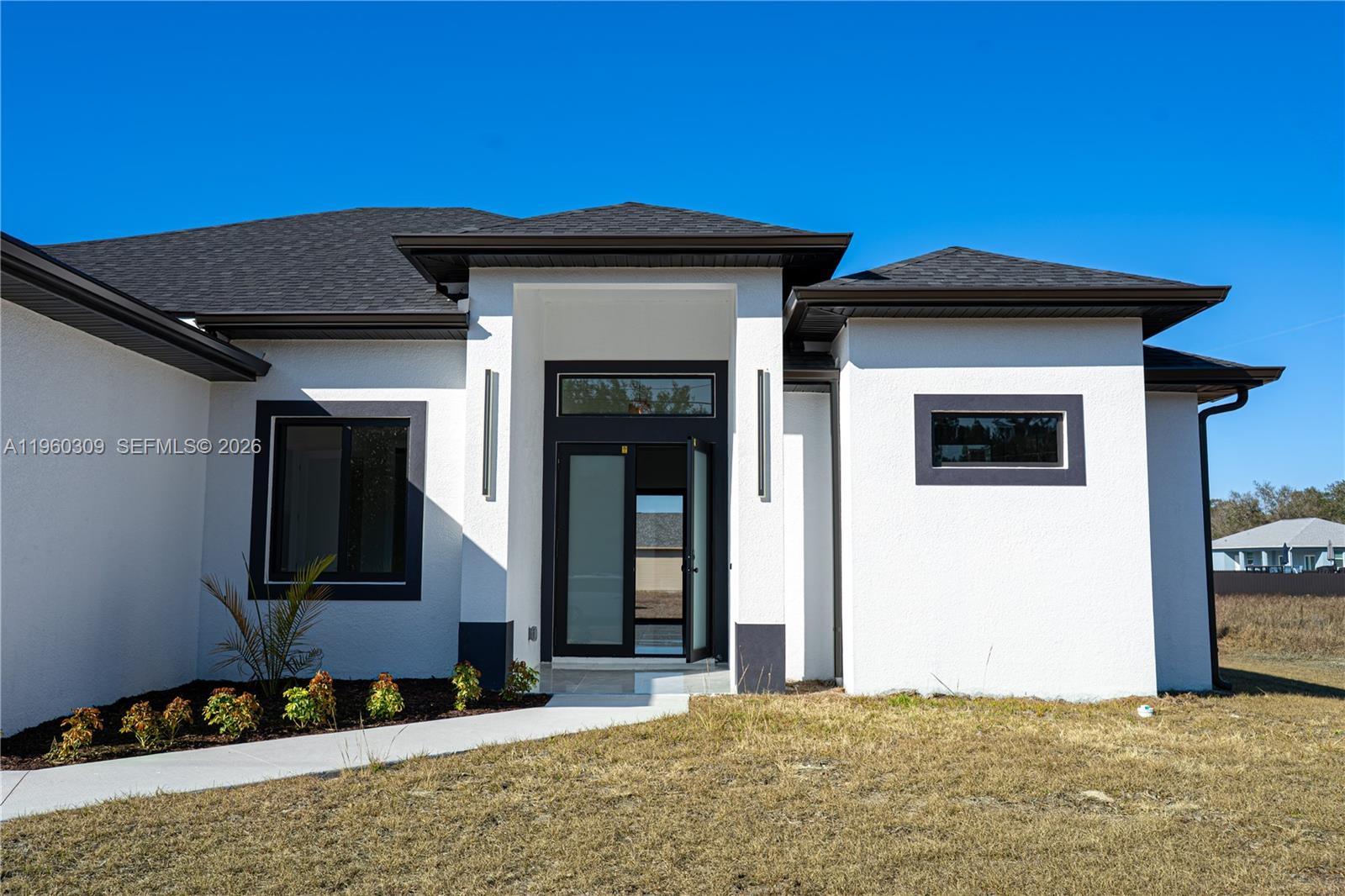The exterior of a modern white house features a dark roof, trim, and glass front door — 2903 E 17th St, Lehigh Acres FL 33972, LEHIGH ACRES, FL