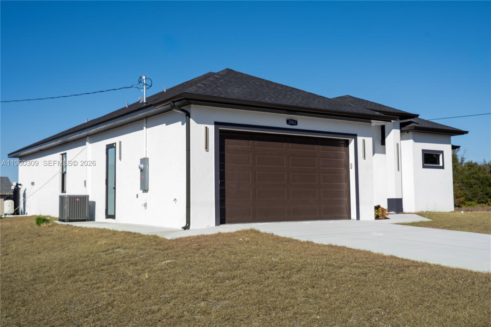 A single-story house with white stucco walls, a dark roof, and a brown garage door — 2903 E 17th St, Lehigh Acres FL 33972, LEHIGH ACRES, FL