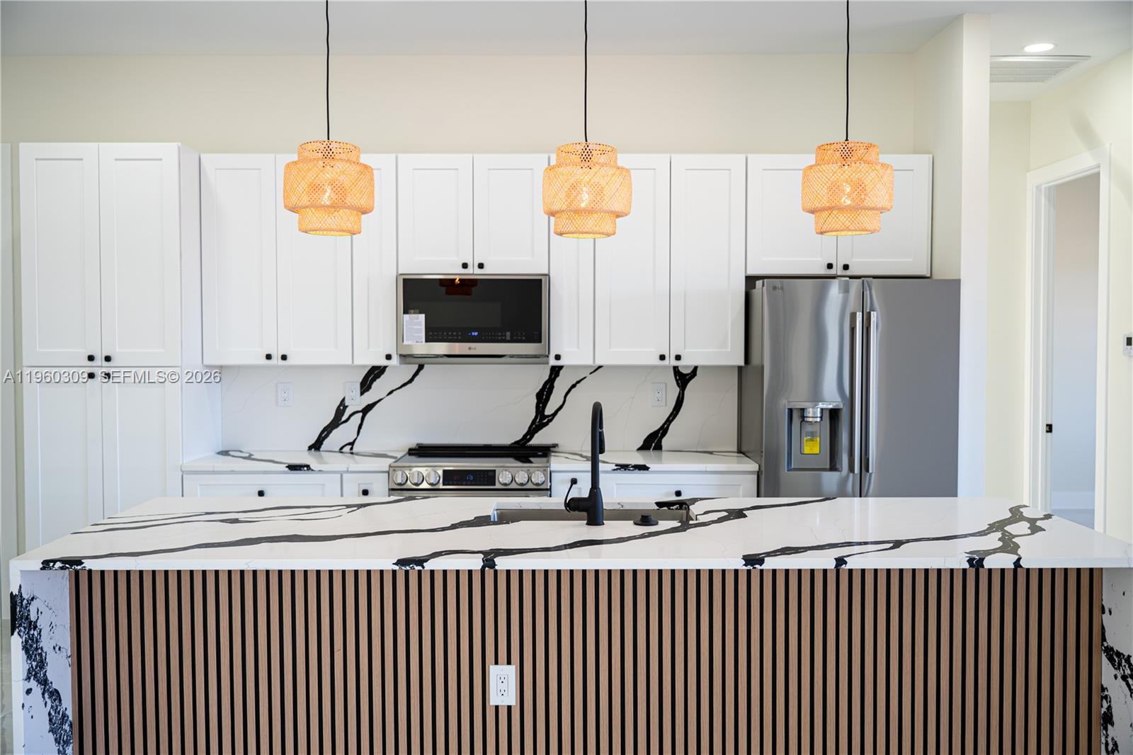 A modern kitchen features white cabinets, a black-veined marble backsplash, and a slatted wood island — 2903 E 17th St, Lehigh Acres FL 33972, LEHIGH ACRES, FL
