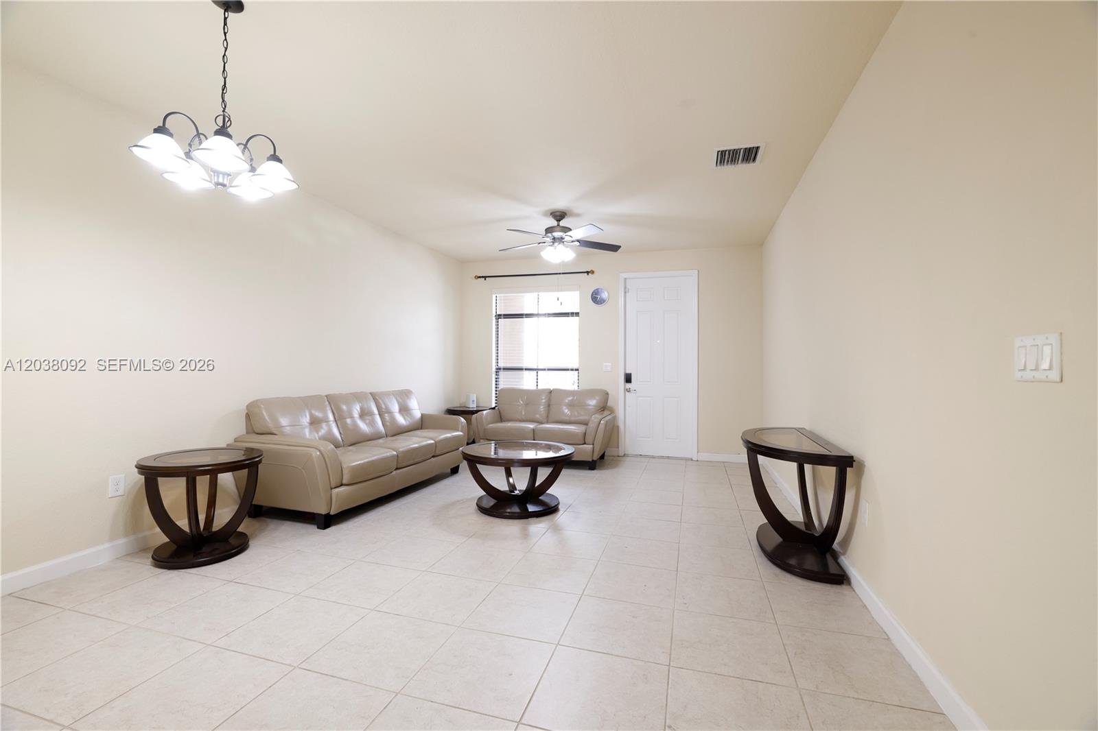 A living room features beige tile floors, two leather sofas, and a dark wood chandelier — 7146 SW 163rd Ave, Miami FL 33193, MIAMI, FL