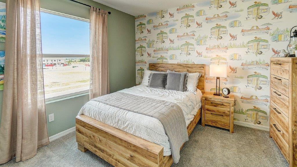 A bedroom features a wooden bed frame, patterned wallpaper, and a window with curtains — 32537 MIDSUMMER NIGHT LANE, WESLEY CHAPEL, FL