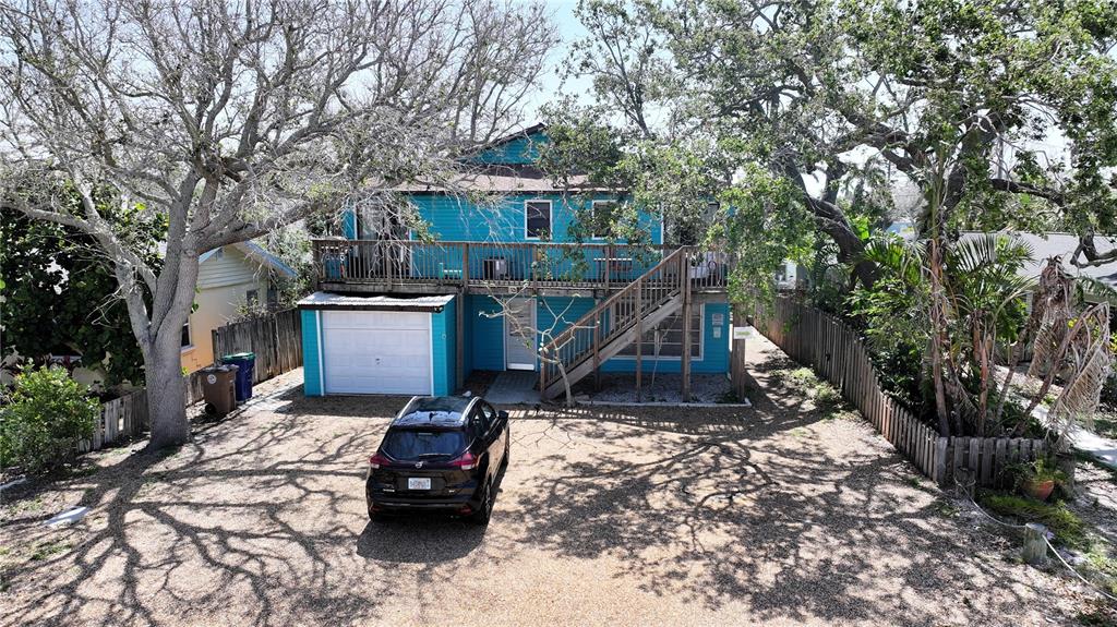 A two-story turquoise house with a wooden deck, exterior staircase, and a gravel driveway — 725 1ST STREET, INDIAN ROCKS BEACH, FL