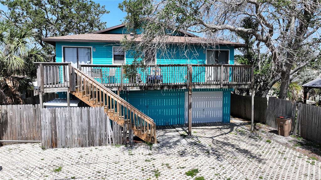 A turquoise elevated house features a wooden deck, an outdoor staircase, and a ground-level garage — 725 1ST STREET, INDIAN ROCKS BEACH, FL