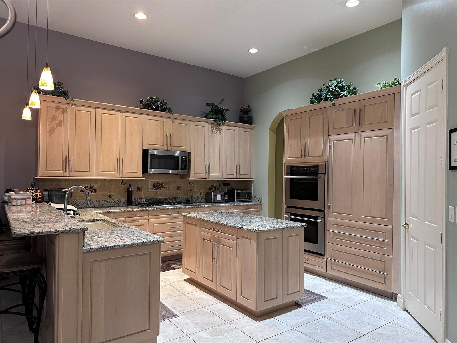 A kitchen features light wood cabinets, granite countertops, a central island, and stainless steel appliances — 8041 E Via Grande, Boynton Beach FL 33437, BOYNTON BEACH, FL