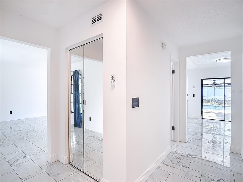 A hallway with white walls and light-colored marble-style tile flooring features a mirrored closet door — 4012 BRAESGATE LANE, TAMPA, FL