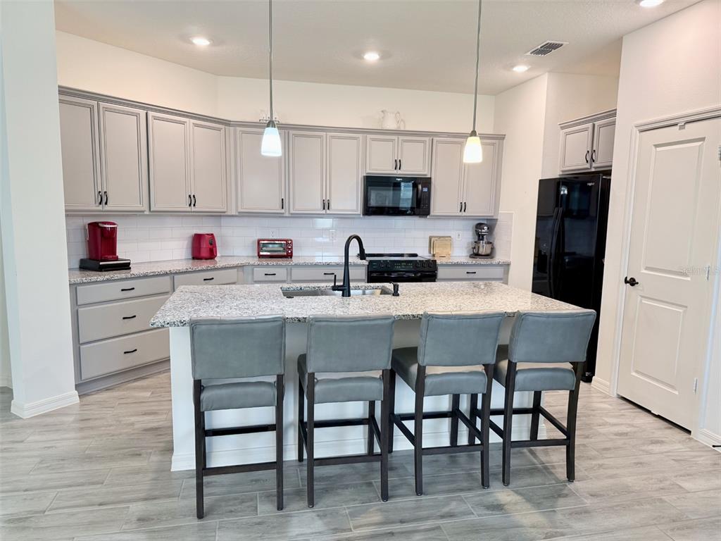A kitchen features gray cabinets, granite countertops, a central island with four chairs, and appliances — 10155 GUTHRIE DRIVE, CLERMONT, FL