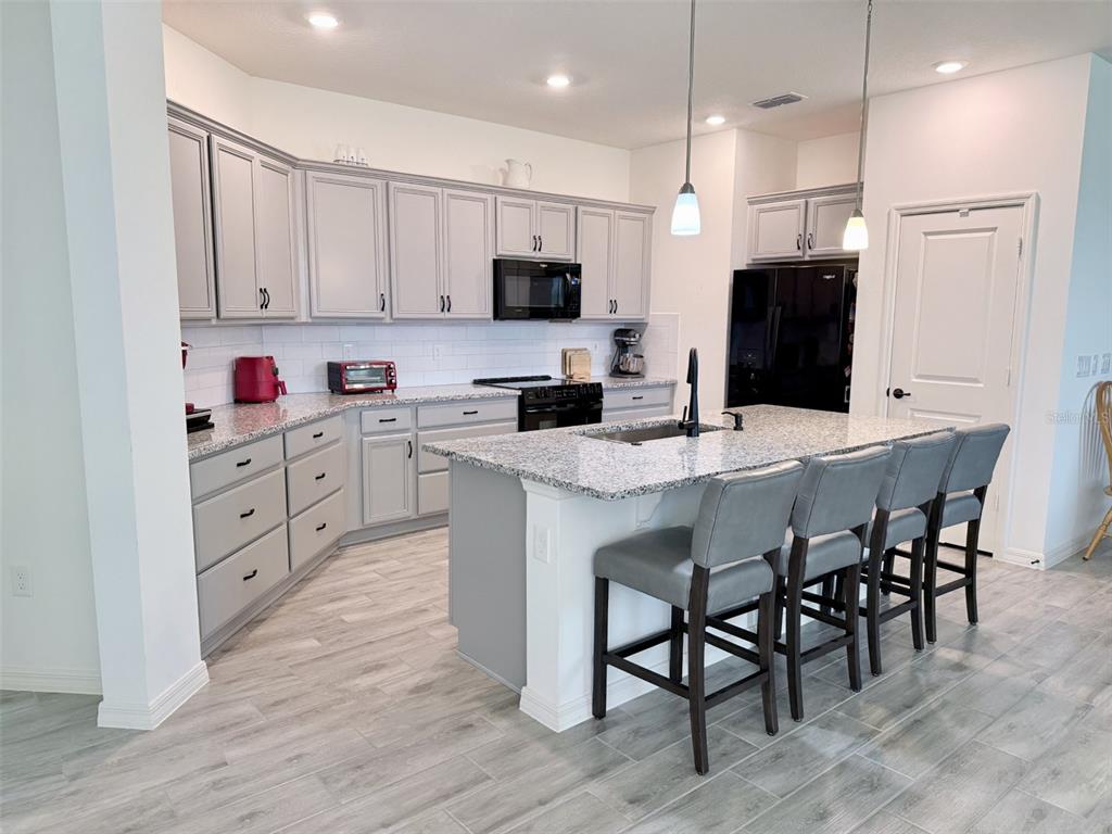 A kitchen features gray cabinets, granite countertops, a central island with seating, and stainless appliances — 10155 GUTHRIE DRIVE, CLERMONT, FL