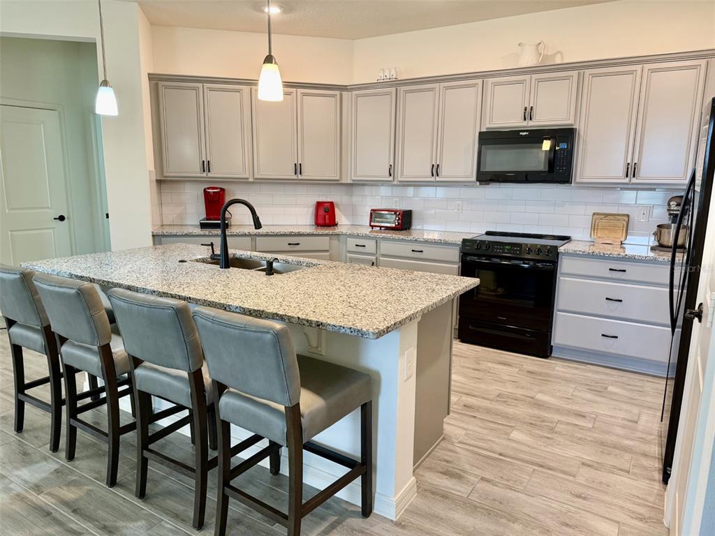A kitchen features gray cabinets, granite countertops, a central island with bar seating, and appliances — 10155 GUTHRIE DRIVE, CLERMONT, FL