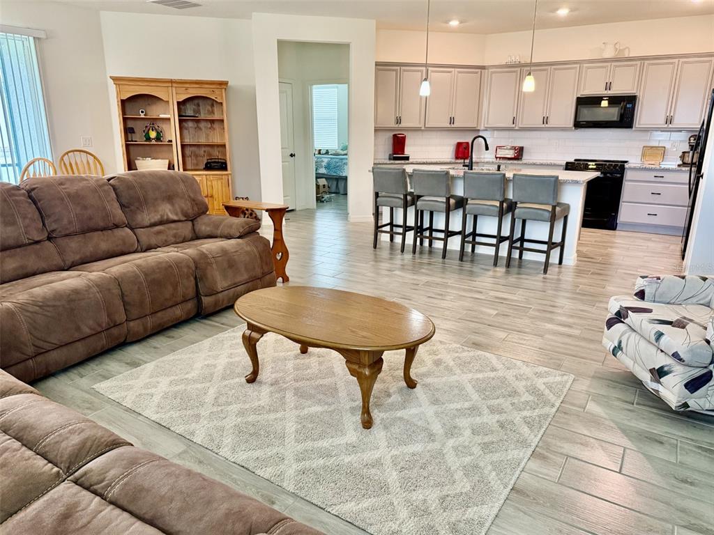 An open-concept living room features a brown sofa, wooden coffee table, and a modern kitchen — 10155 GUTHRIE DRIVE, CLERMONT, FL