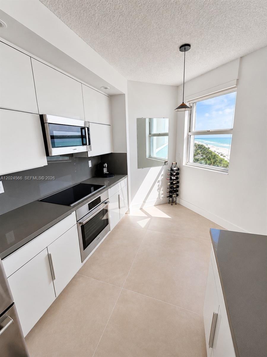 A modern kitchen features white cabinets, gray countertops, and a window overlooking the ocean — 4201 Collins Ave # 1503, Miami Beach FL 33140, MIAMI BEACH, FL