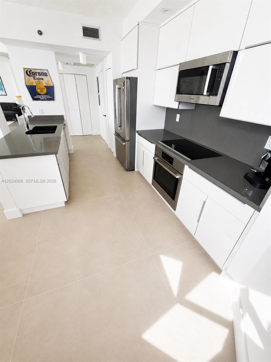 A modern kitchen features white cabinetry, stainless steel appliances, and dark gray countertops — 4201 Collins Ave # 1503, Miami Beach FL 33140, MIAMI BEACH, FL
