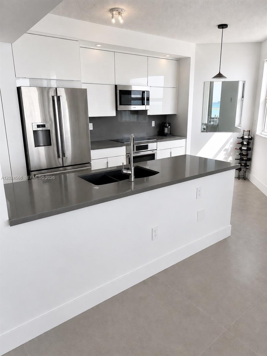 A modern kitchen features white cabinets, stainless steel appliances, and a gray quartz island countertop — 4201 Collins Ave # 1503, Miami Beach FL 33140, MIAMI BEACH, FL