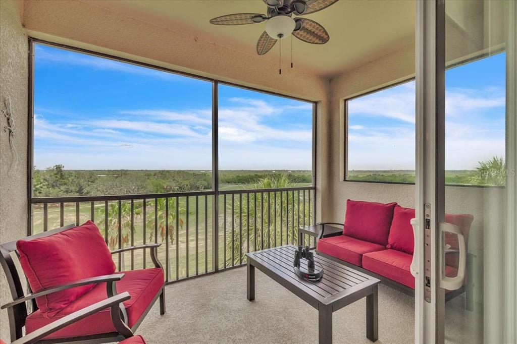 A screened-in balcony features red cushioned furniture, a coffee table, and a ceiling fan — 7607 GRAND ESTUARY TRAIL UNIT 406, BRADENTON, FL
