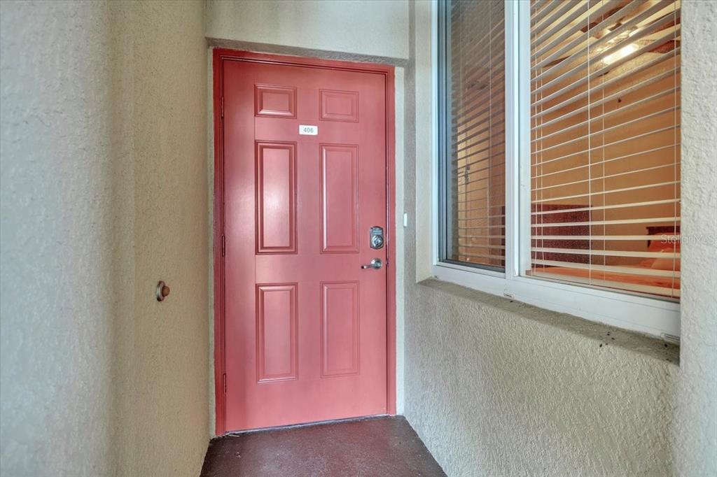 A red front door with the number 406 is situated next to a window with blinds — 7607 GRAND ESTUARY TRAIL UNIT 406, BRADENTON, FL
