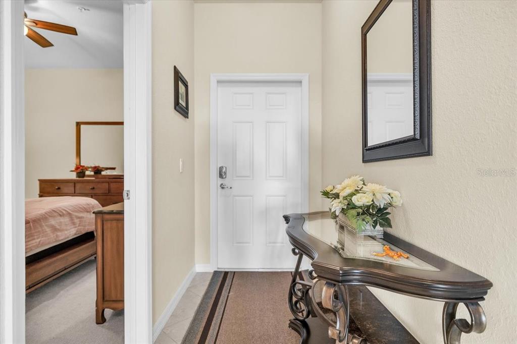 An entryway features a white door, a dark console table with flowers, and a mirror — 7607 GRAND ESTUARY TRAIL UNIT 406, BRADENTON, FL