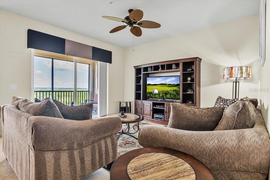 A living room features a television in a wooden entertainment center and a ceiling fan — 7607 GRAND ESTUARY TRAIL UNIT 406, BRADENTON, FL