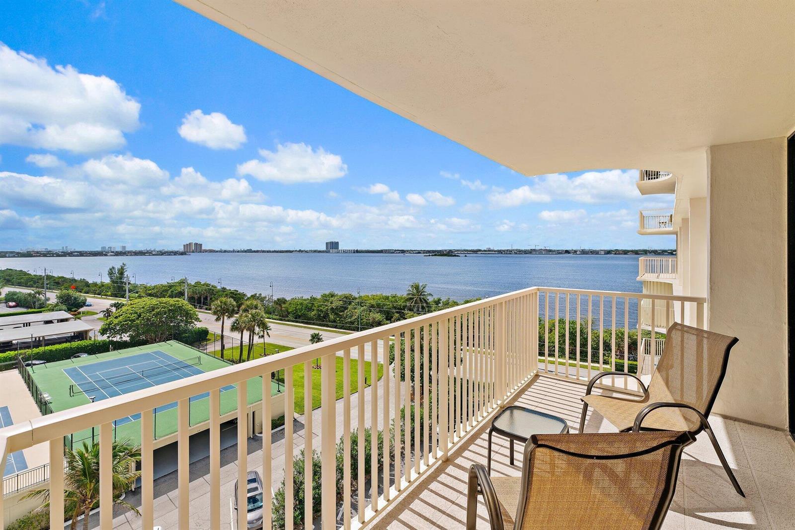 A balcony with two chairs overlooks a tennis court, a road, and a large body of water — 5480 N Ocean Drive, Singer Island FL 33404, SINGER ISLAND, FL